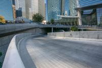 an empty parking area with cars and buildings in the background on a city street between a concrete wall and a sidewalk