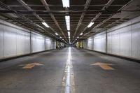 an empty parking garage with an arrow painted on the floor and light fixtures above it