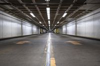 an empty parking garage with an arrow painted on the floor and light fixtures above it