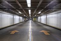 an empty parking garage with an arrow painted on the floor and light fixtures above it