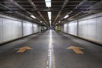 an empty parking garage with an arrow painted on the floor and light fixtures above it