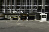 a parking garage with a sign for the parking garage at an empty parking lot between two tall buildings