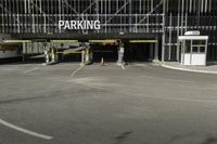 a parking garage with a sign for the parking garage at an empty parking lot between two tall buildings