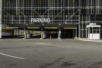 a parking garage with a sign for the parking garage at an empty parking lot between two tall buildings