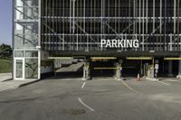 a parking garage with a sign for the parking garage at an empty parking lot between two tall buildings