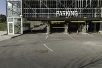 a parking garage with a sign for the parking garage at an empty parking lot between two tall buildings