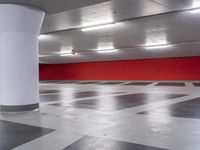 an empty parking garage with red wall and white columns, empty parking garage floor, large white column, and black and white