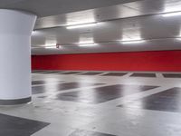 an empty parking garage with red wall and white columns, empty parking garage floor, large white column, and black and white