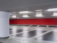 an empty parking garage with red wall and white columns, empty parking garage floor, large white column, and black and white