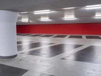 an empty parking garage with red wall and white columns, empty parking garage floor, large white column, and black and white