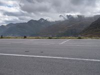 an empty parking lot on the side of the mountain with mountains and fog covered mountains around it