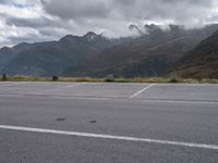 an empty parking lot on the side of the mountain with mountains and fog covered mountains around it