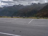 an empty parking lot on the side of the mountain with mountains and fog covered mountains around it