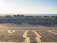 an empty parking lot with sand and water on the side of a beach near the ocean