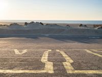 an empty parking lot with sand and water on the side of a beach near the ocean