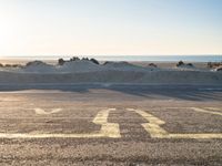 an empty parking lot with sand and water on the side of a beach near the ocean