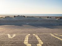 an empty parking lot with sand and water on the side of a beach near the ocean