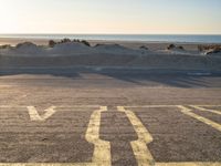 an empty parking lot with sand and water on the side of a beach near the ocean