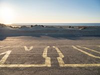 an empty parking lot with sand and water on the side of a beach near the ocean