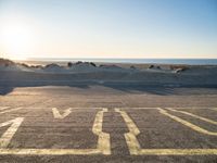 an empty parking lot with sand and water on the side of a beach near the ocean