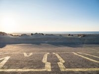 an empty parking lot with sand and water on the side of a beach near the ocean