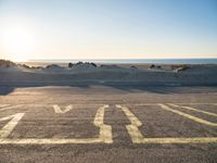 an empty parking lot with sand and water on the side of a beach near the ocean