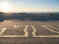 an empty parking lot with sand and water on the side of a beach near the ocean