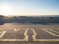 an empty parking lot with sand and water on the side of a beach near the ocean