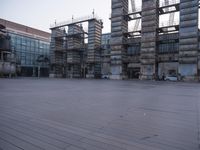 a photo of an empty parking lot with multiple stacks of buildings in the background while there is some smoke coming out from them
