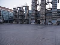 a photo of an empty parking lot with multiple stacks of buildings in the background while there is some smoke coming out from them