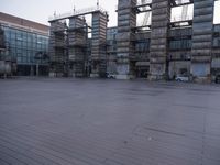 a photo of an empty parking lot with multiple stacks of buildings in the background while there is some smoke coming out from them