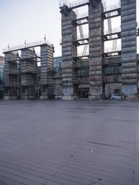 a photo of an empty parking lot with multiple stacks of buildings in the background while there is some smoke coming out from them