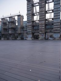 a photo of an empty parking lot with multiple stacks of buildings in the background while there is some smoke coming out from them
