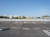 empty parking lot with buildings in the background and white lines painted on asphalt between sides