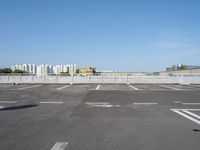 empty parking lot with buildings in the background and white lines painted on asphalt between sides