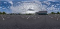 a wide angle view shows an empty parking lot with trees on both sides and clouds in the sky above