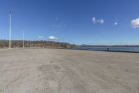 the parking lot is empty with blue skies above it and water in front of trees