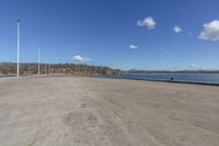 the parking lot is empty with blue skies above it and water in front of trees