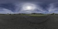 the wide lens of an empty parking lot shows a blue sky and some clouds in front of the sun