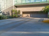 an empty parking lot in front of a building with multiple potted plants on the sidewalk