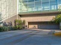 an empty parking lot in front of a building with multiple potted plants on the sidewalk