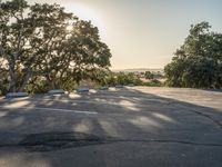 a empty parking lot with two cars in the background and trees on both sides of the parking lot