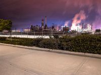 an empty parking lot with some power plants behind it on a stormy day at night