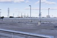 an empty parking lot with white fence and street lights in the background on the road