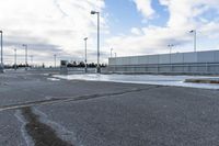 an empty parking lot with snow, ice and electric poles in the background of a wall