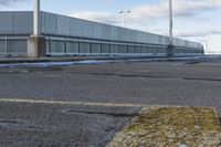 an empty parking lot with snow, ice and electric poles in the background of a wall