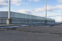 an empty parking lot with snow, ice and electric poles in the background of a wall