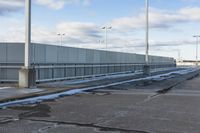 an empty parking lot with snow, ice and electric poles in the background of a wall