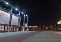 an empty parking lot at night with lights on the building's side and a parking area at the end