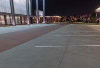 an empty parking lot at night with lights on the building's side and a parking area at the end